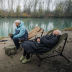 zwei Personen in Campingstühlen an einem See